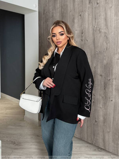 Woman in a black blazer with 'La La' logo, holding a white handbag against a wooden wall.