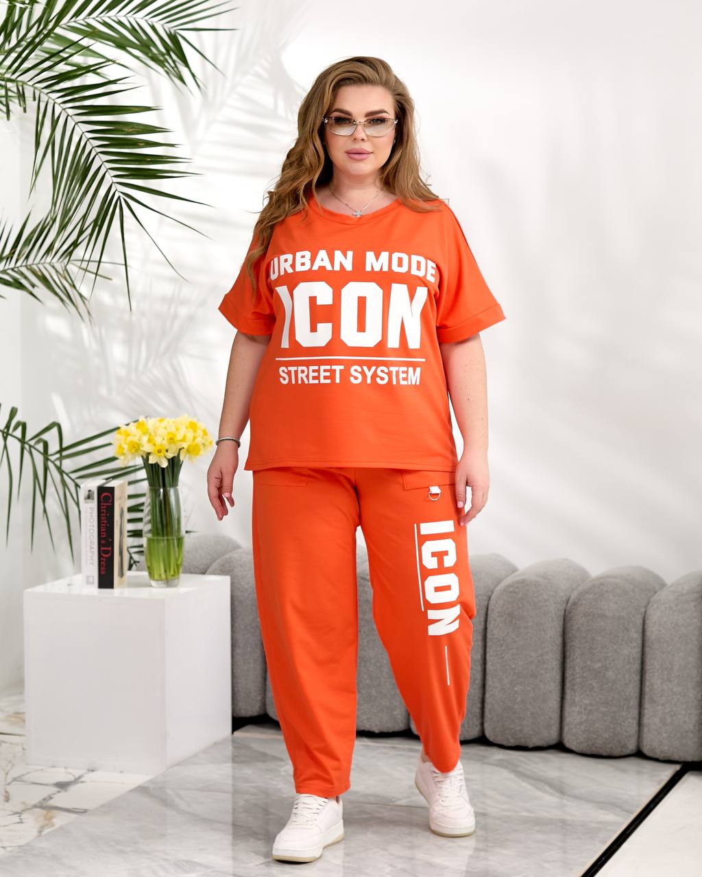 Woman wearing an orange 'ICON' outfit in a modern living room setting