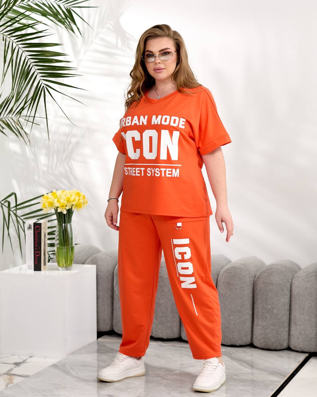 Woman wearing an orange 'ICON' outfit in a modern living room.