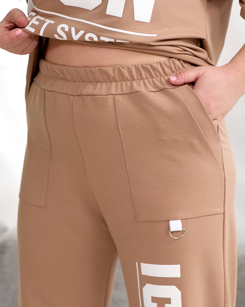 Brown pants with white text and a belt buckle on a neutral background