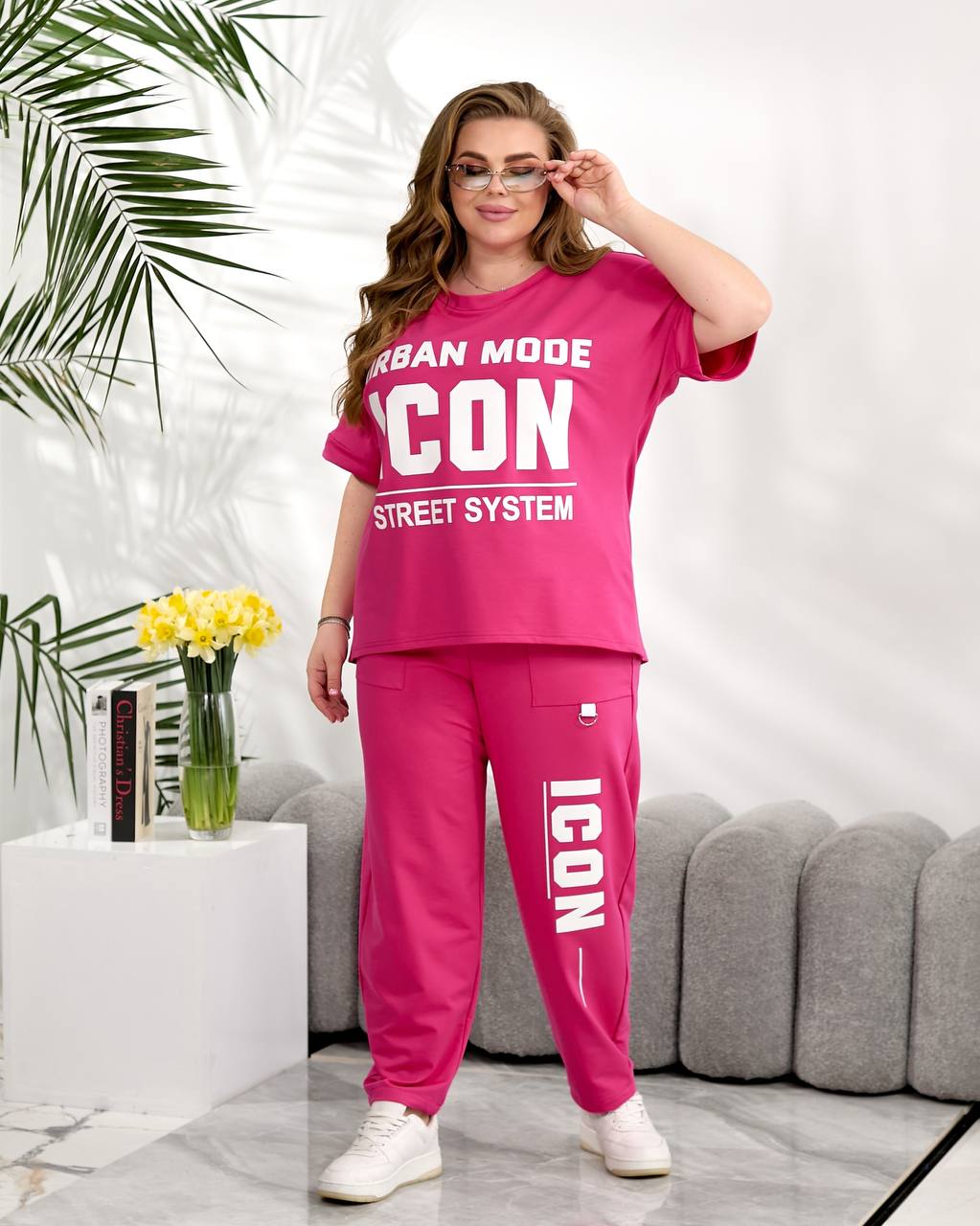 Woman wearing a pink 'ICON' outfit in a modern living room setting