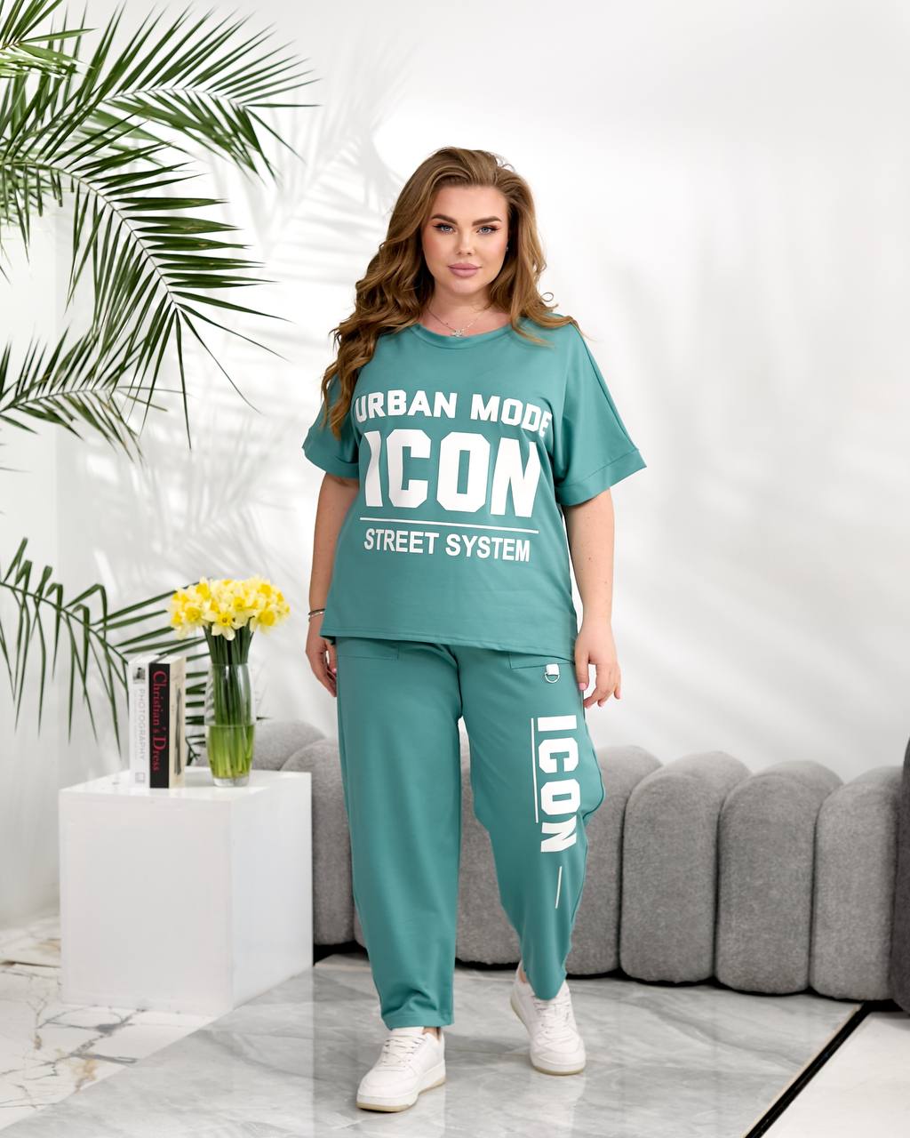 Woman wearing a teal 'ICON' outfit in a modern living room.