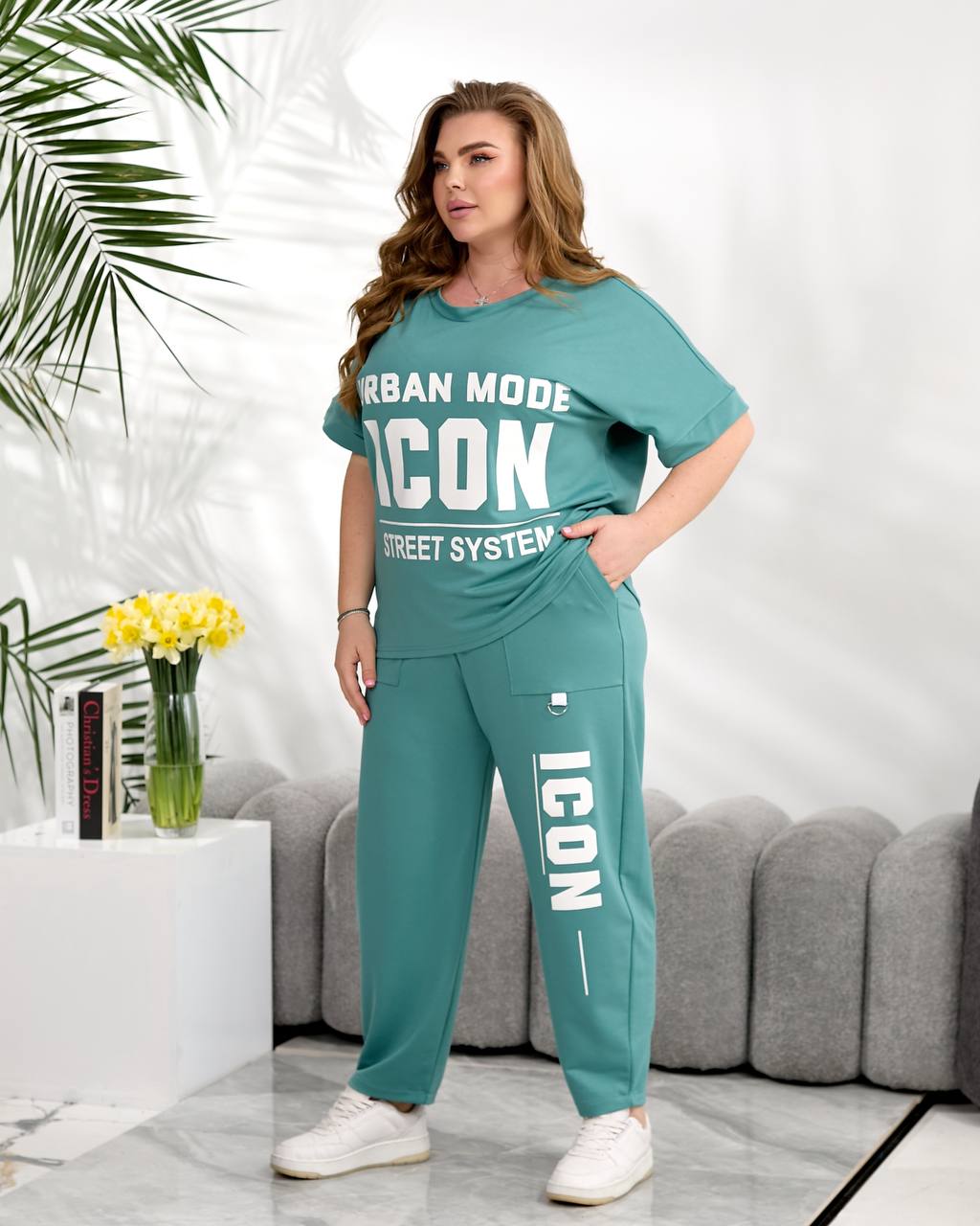 Woman wearing a teal 'ICON' outfit in a living room setting