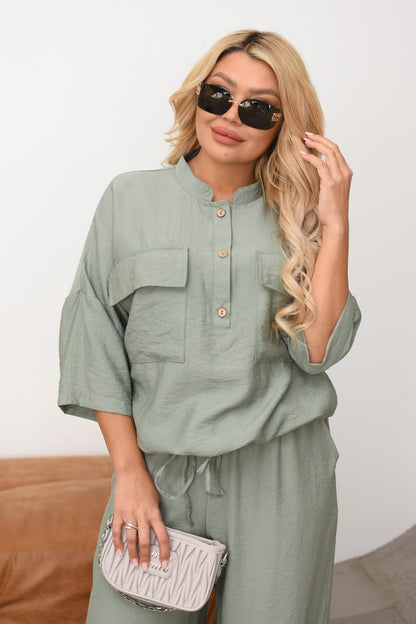 Woman wearing a green outfit with sunglasses and a white clutch against a plain background