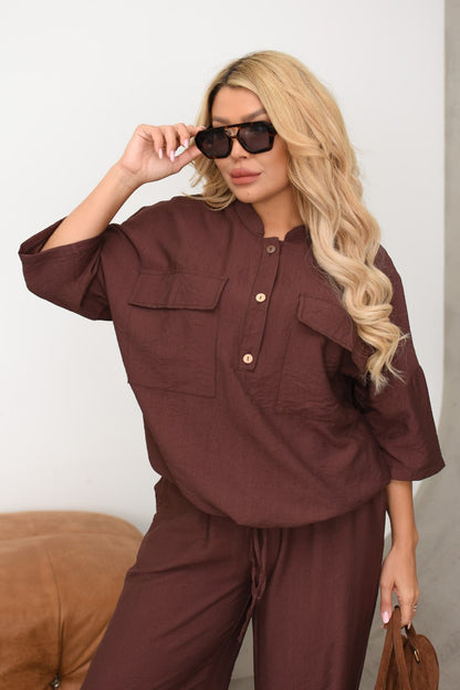 Woman wearing a brown outfit with sunglasses and a handbag against a neutral background