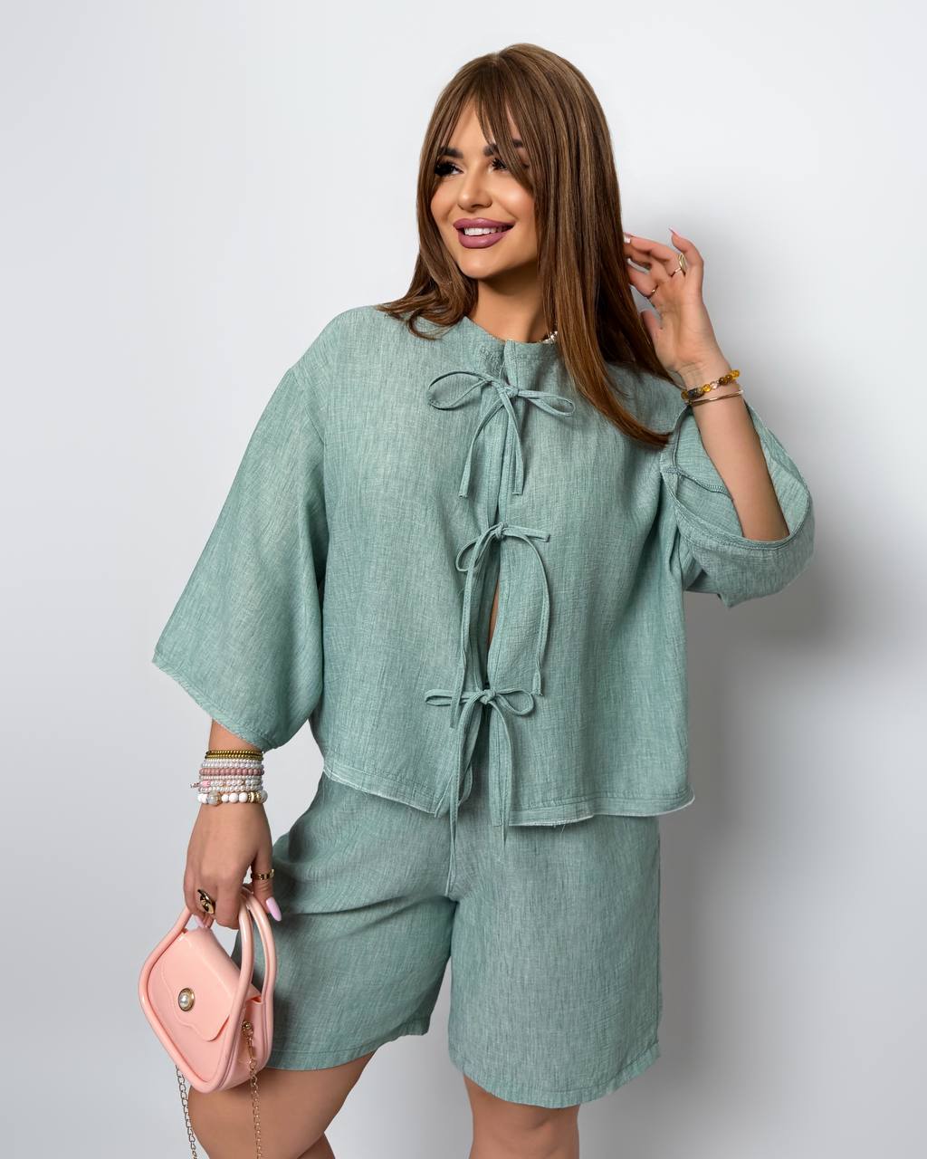 Woman wearing a green outfit with a pink handbag on a white background