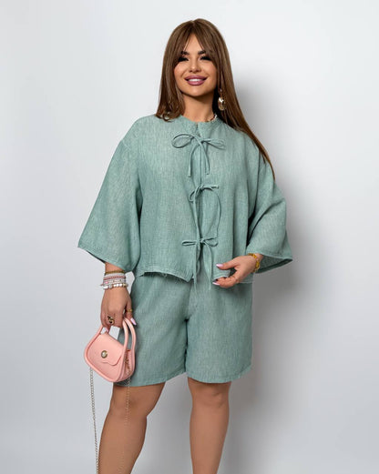 Woman wearing a green outfit with a pink handbag against a light gray background