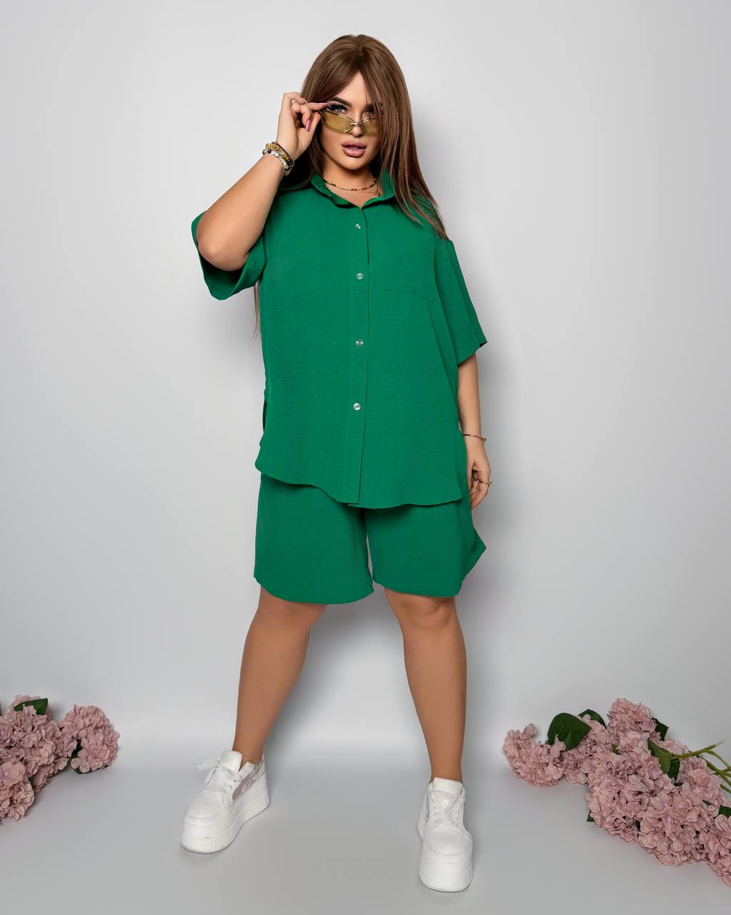 Woman wearing a green outfit with white sneakers on a light gray background