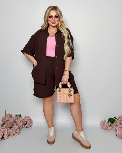 Woman in a brown outfit with pink top and shoes, holding a beige handbag on a light gray background.