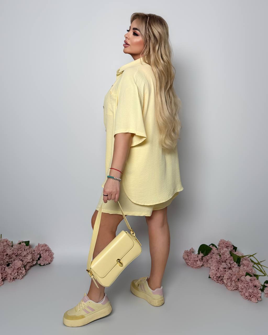 Woman in a yellow outfit holding a matching handbag against a light gray background with pink flowers.