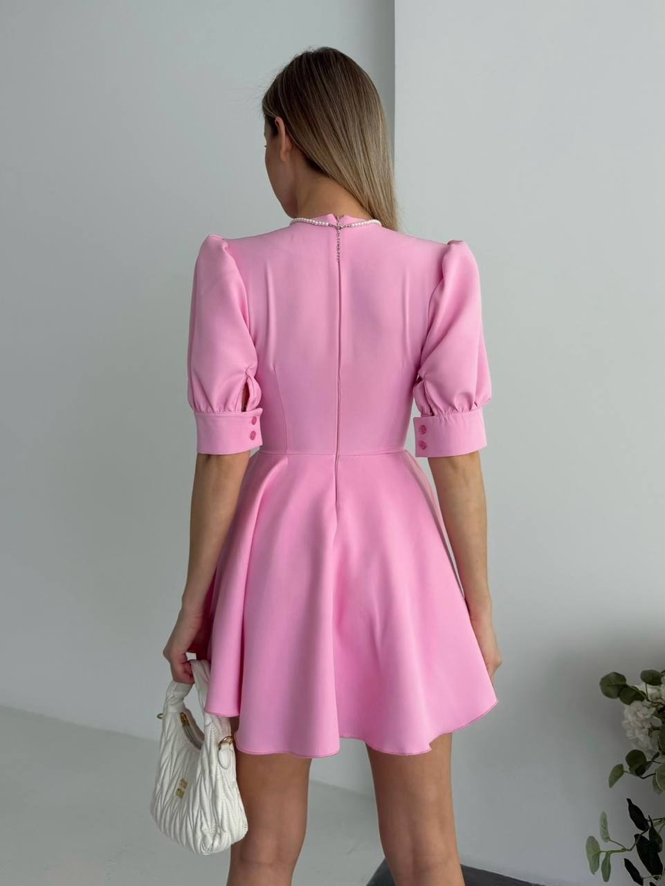Woman wearing a pink dress with puff sleeves against a plain background