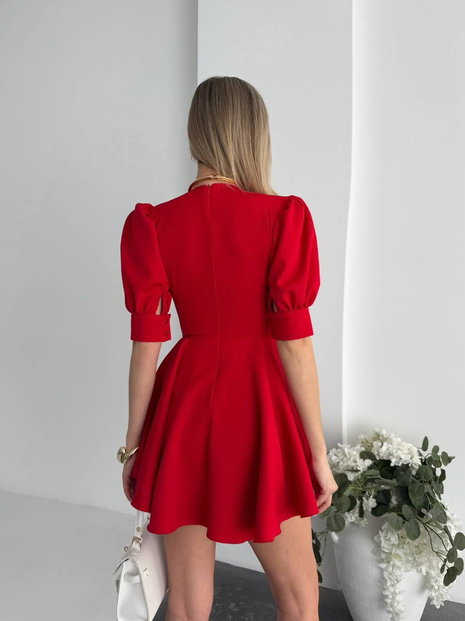 Woman wearing a red dress with puff sleeves in a minimal indoor setting.