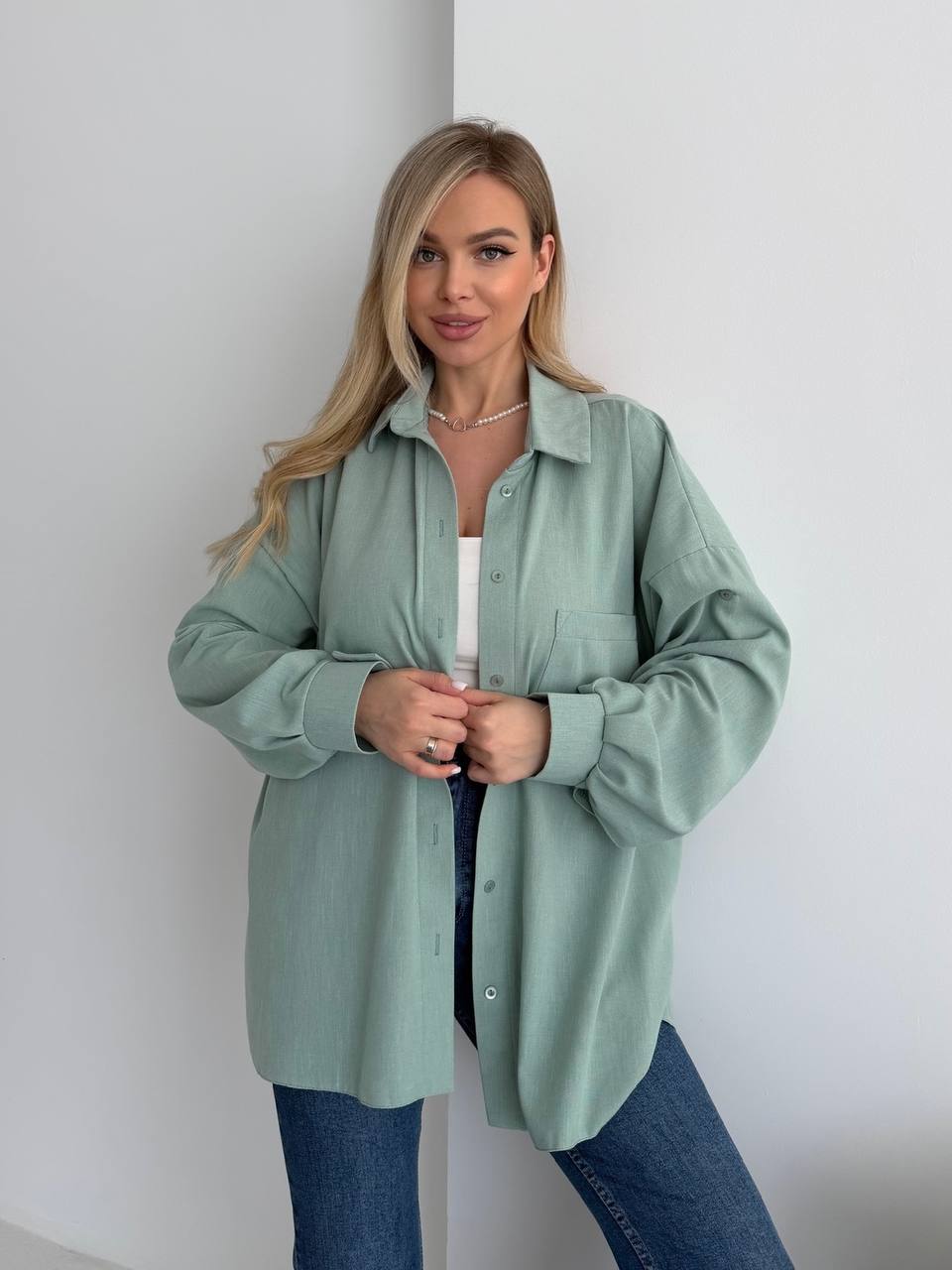 Woman wearing a light green shirt and blue jeans against a white background