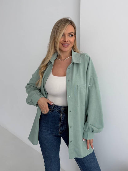 Woman wearing a light green shirt over a white top and blue jeans against a plain background