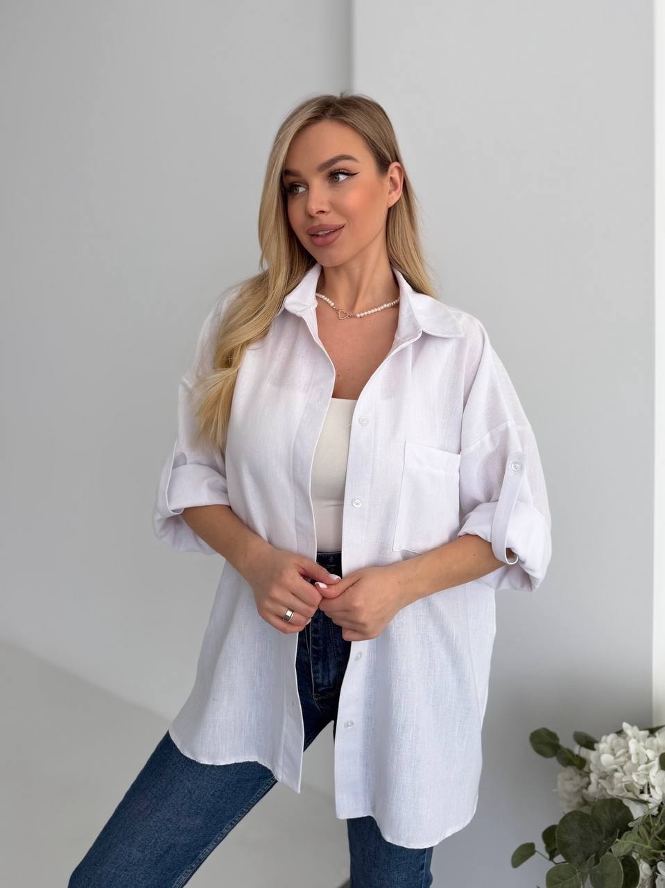 Woman wearing a white shirt and blue jeans against a plain background