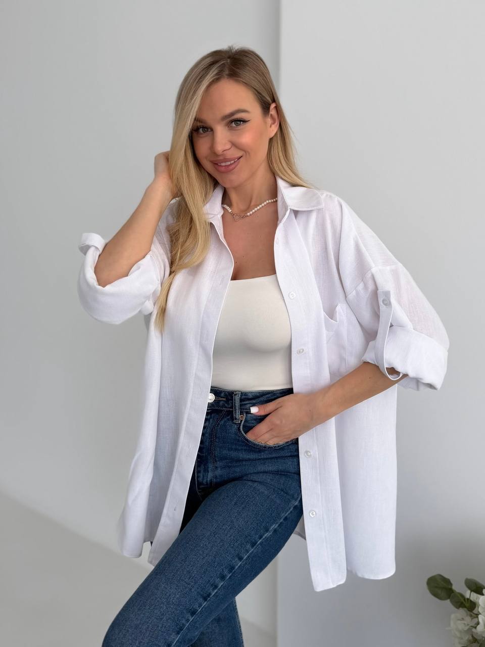 Woman wearing a white shirt over a white top and blue jeans against a plain background
