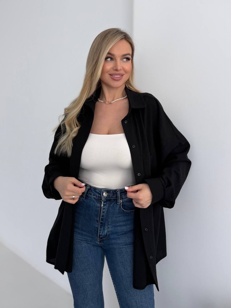 Woman wearing a black shirt over a white top and blue jeans on a plain background