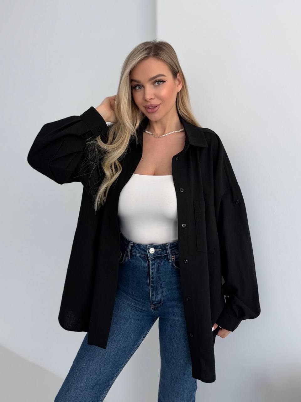 Woman wearing a black oversized shirt, white top, and blue jeans against a plain background