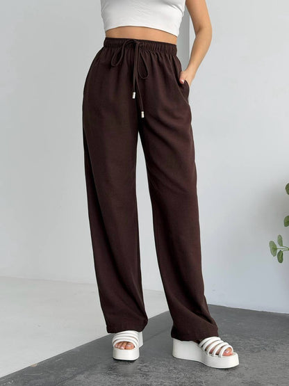 Brown wide-leg pants worn by a person on a gray floor with a white wall background