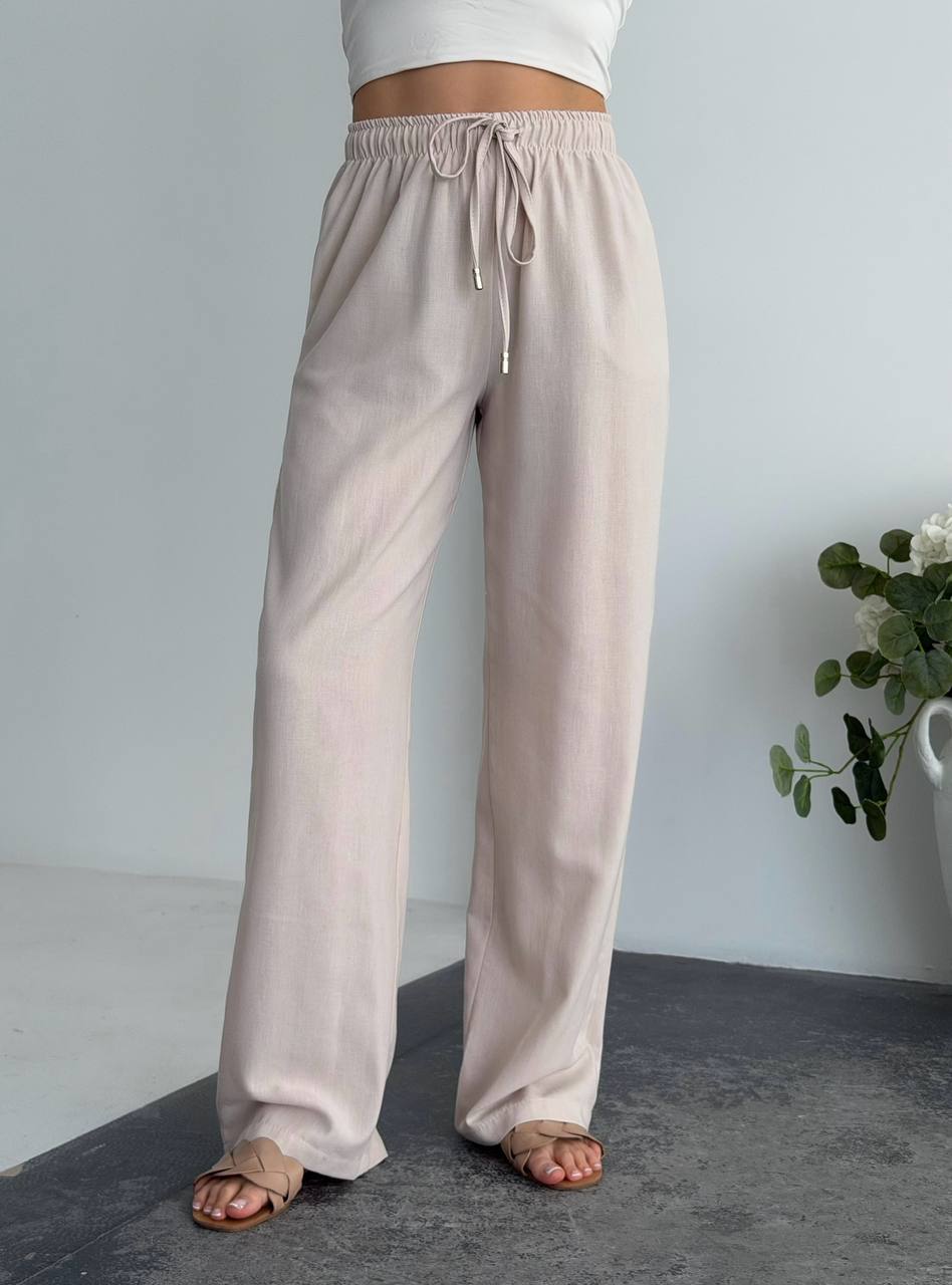 Beige wide-leg pants worn by a person on a neutral background with a plant.
