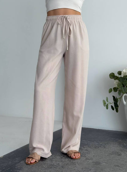 Beige wide-leg pants worn by a person on a neutral background with a plant.