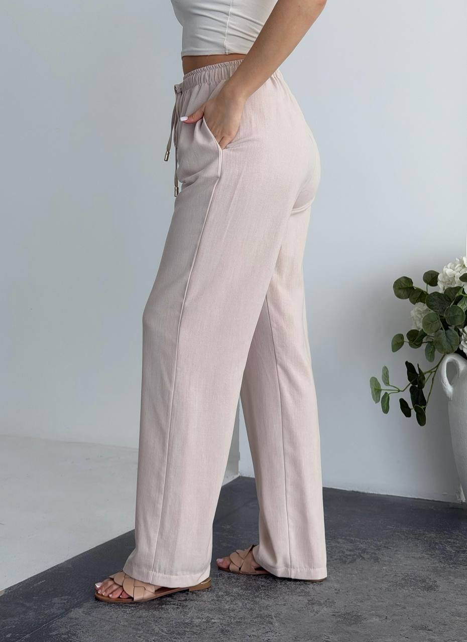 Person wearing light pink wide-leg pants with a neutral background