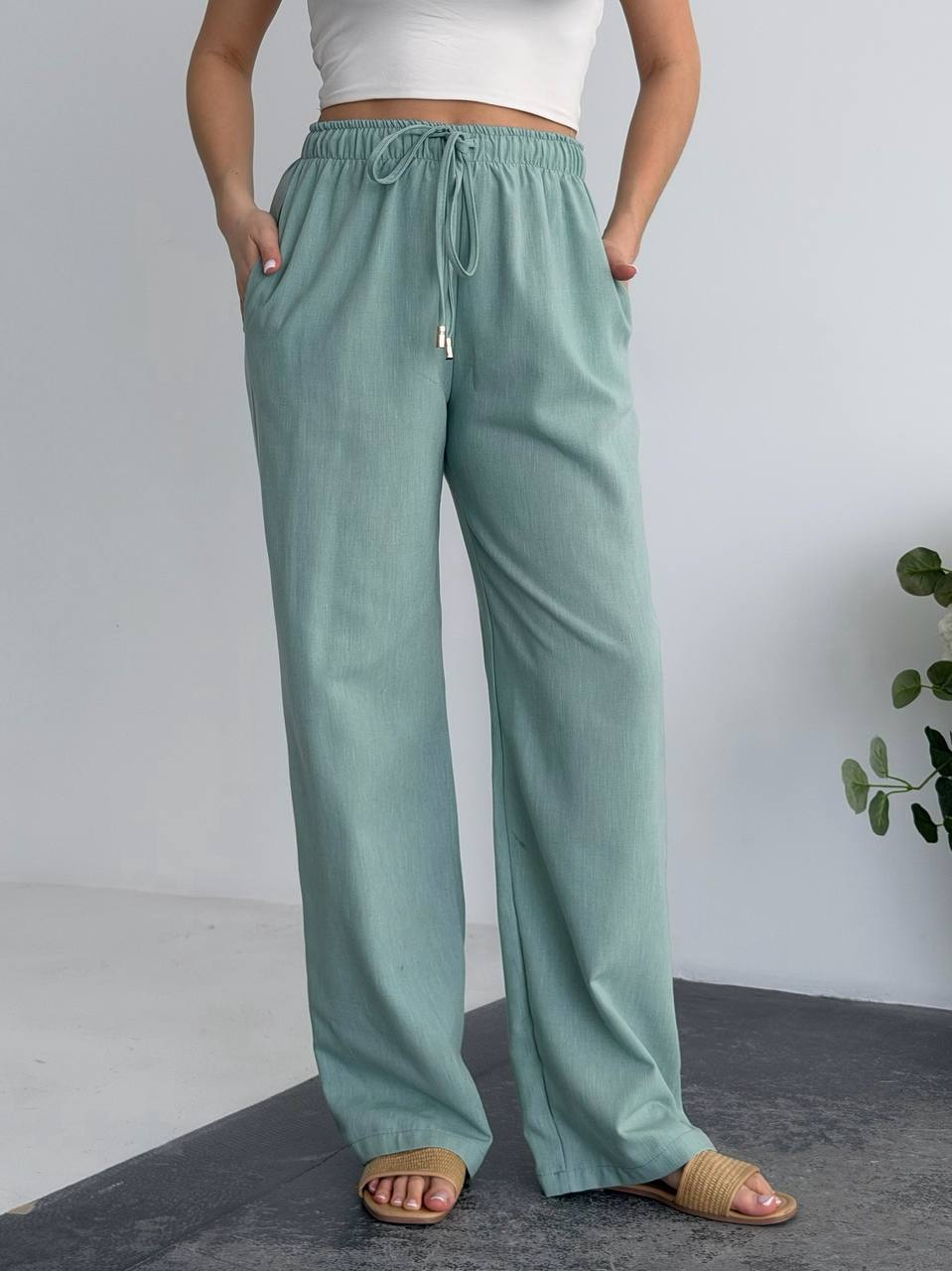 Person wearing teal pants with a white top on a gray background