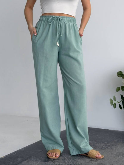 Person wearing teal pants with a white top on a gray background