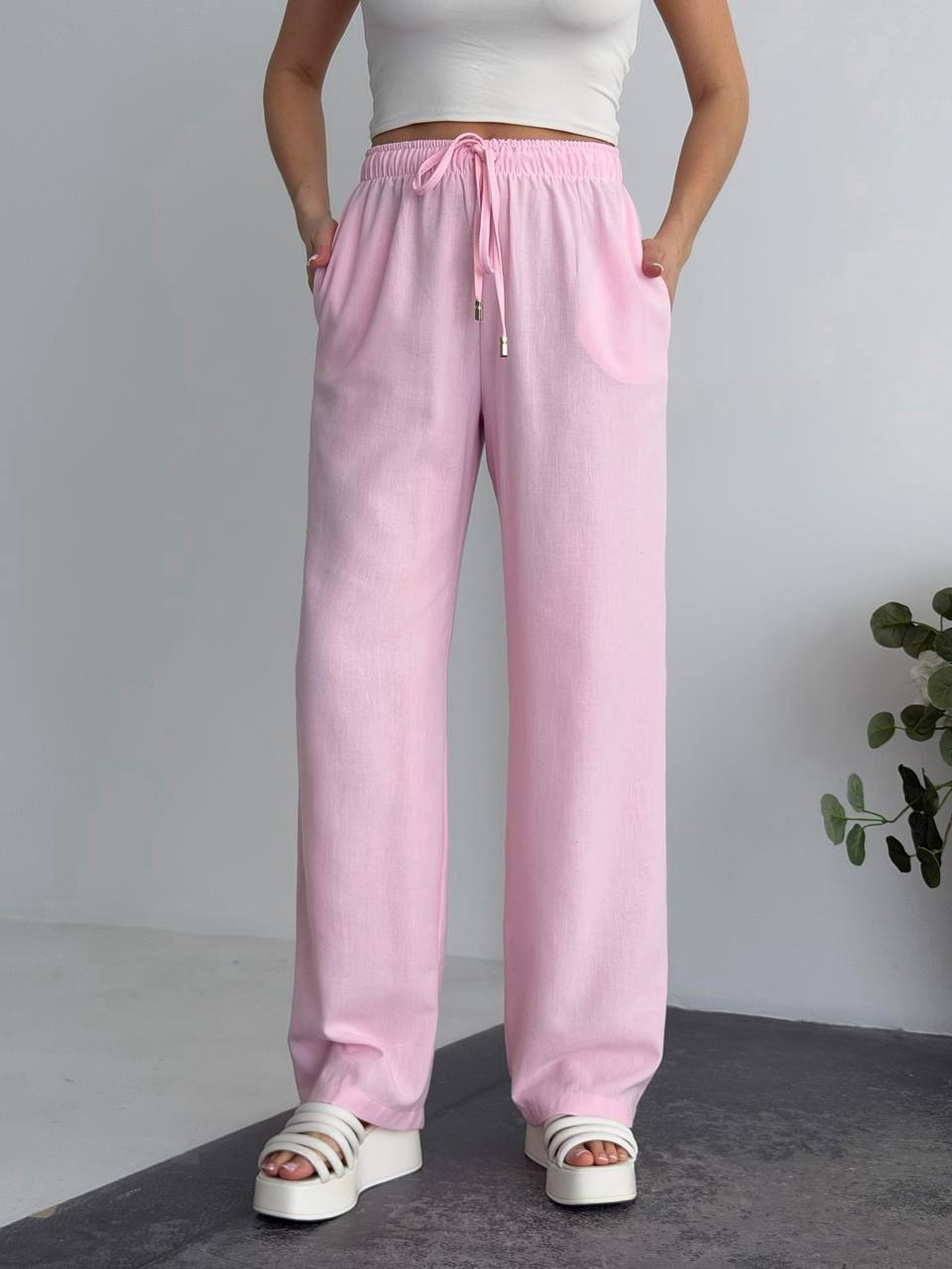 Person wearing pink sweatpants with a white top and sandals on a gray floor.