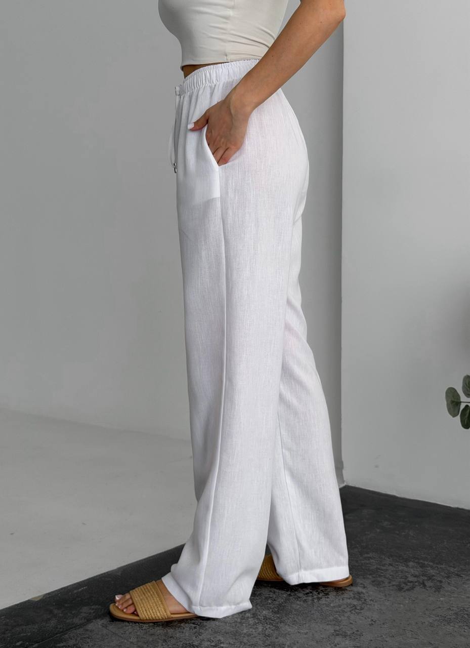 Person wearing white wide-leg pants against a gray background