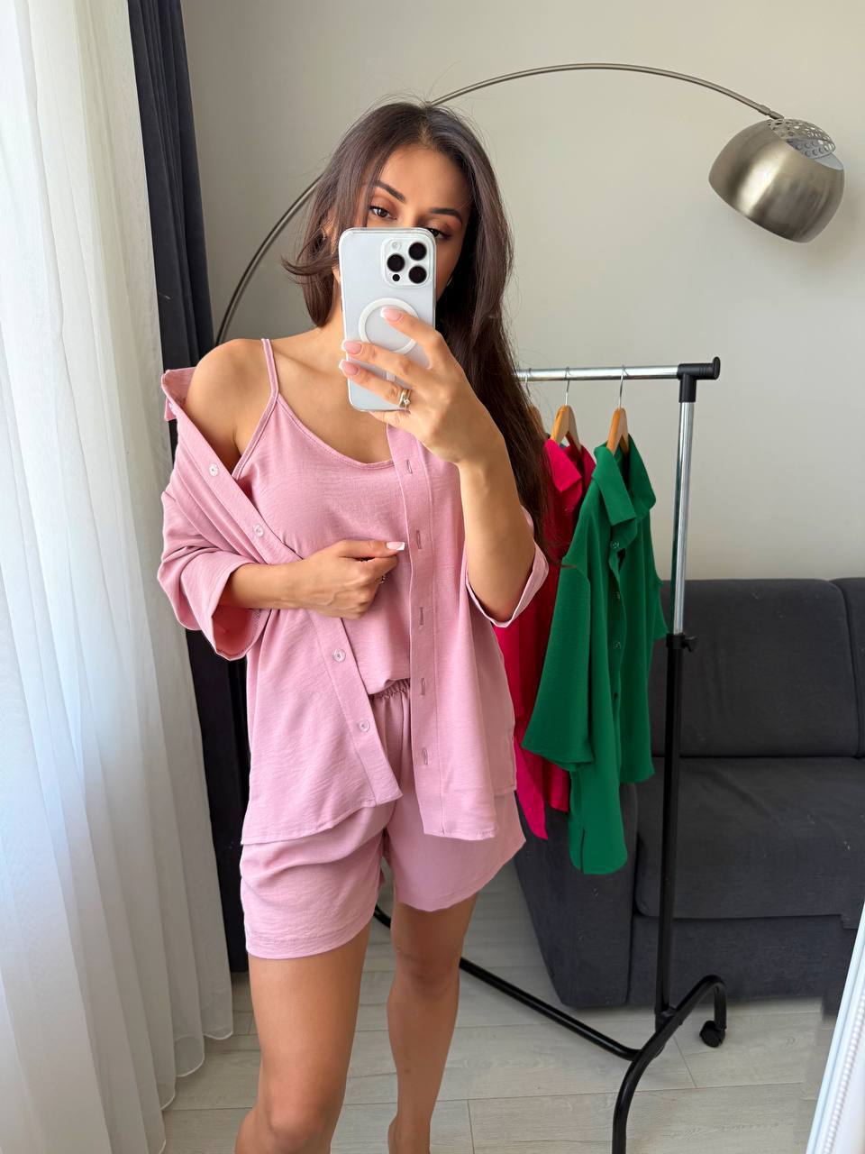 Woman taking a mirror selfie wearing a pink outfit in a room with a coat rack and gray sofa.