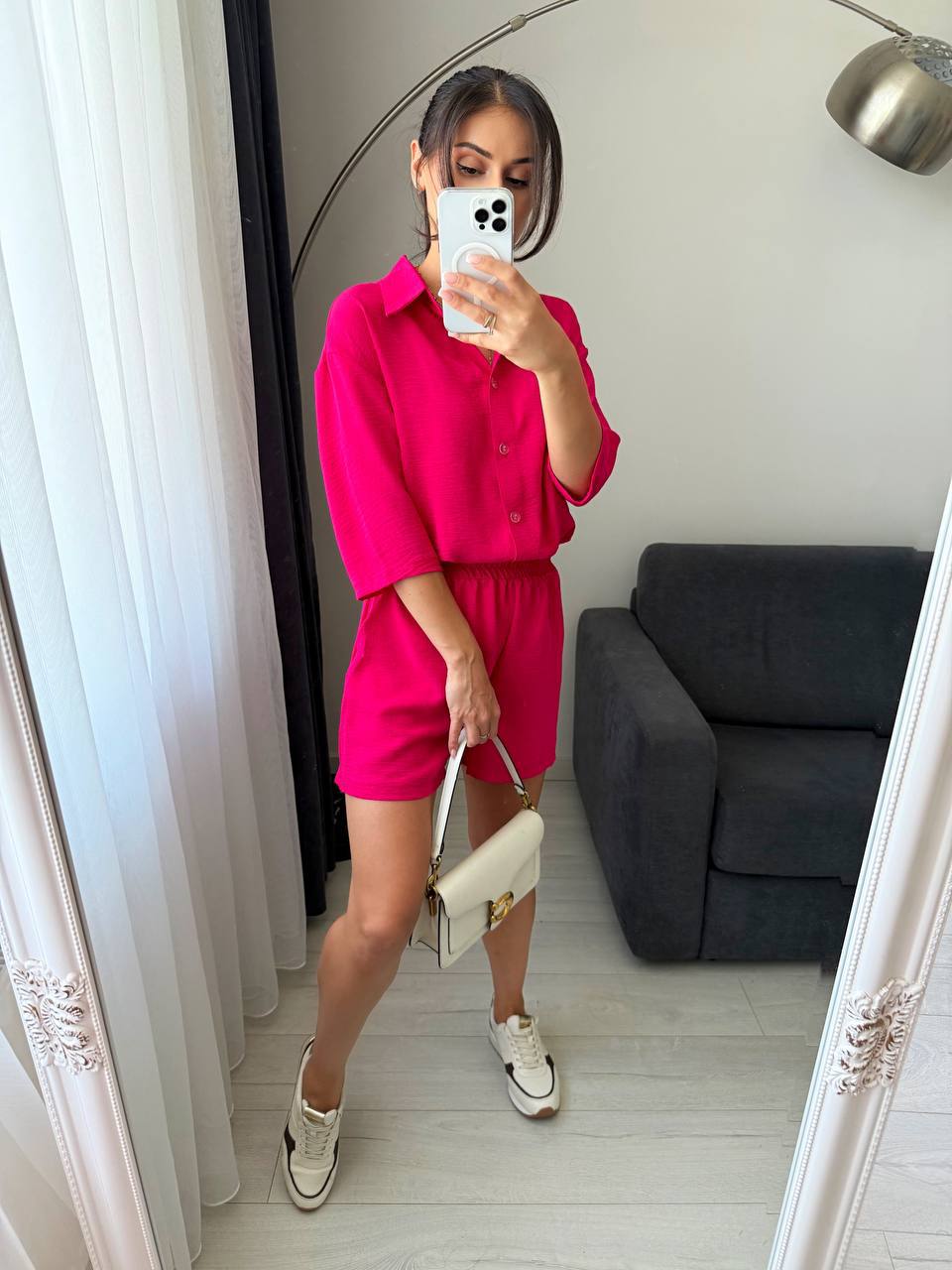 Person wearing a bright pink outfit taking a mirror selfie in a room.