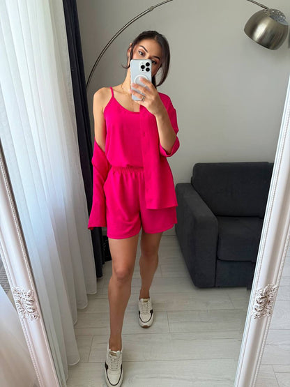 Person wearing a bright pink outfit taking a mirror selfie in a room with a gray sofa.