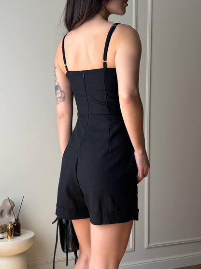 Person wearing a black romper with thin straps in a neutral setting