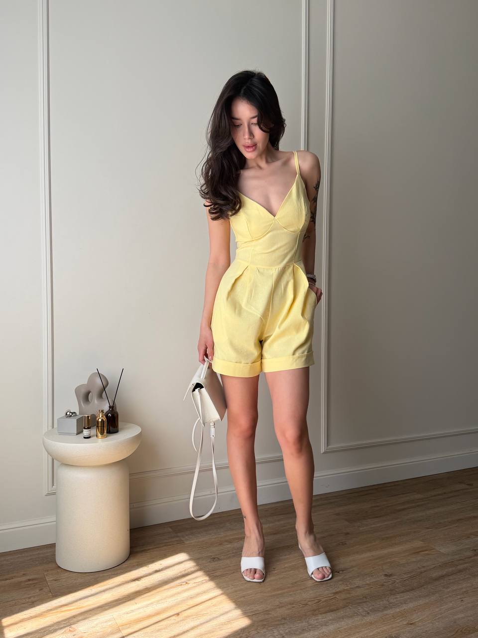 Woman in a yellow jumpsuit standing in a room with a white wall and wooden floor.