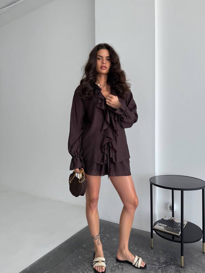 Woman in a dark brown outfit standing in a minimalistic room with a small table.