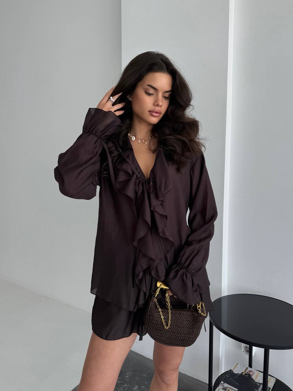 Woman wearing a dark brown ruffled blouse and shorts in an indoor setting.