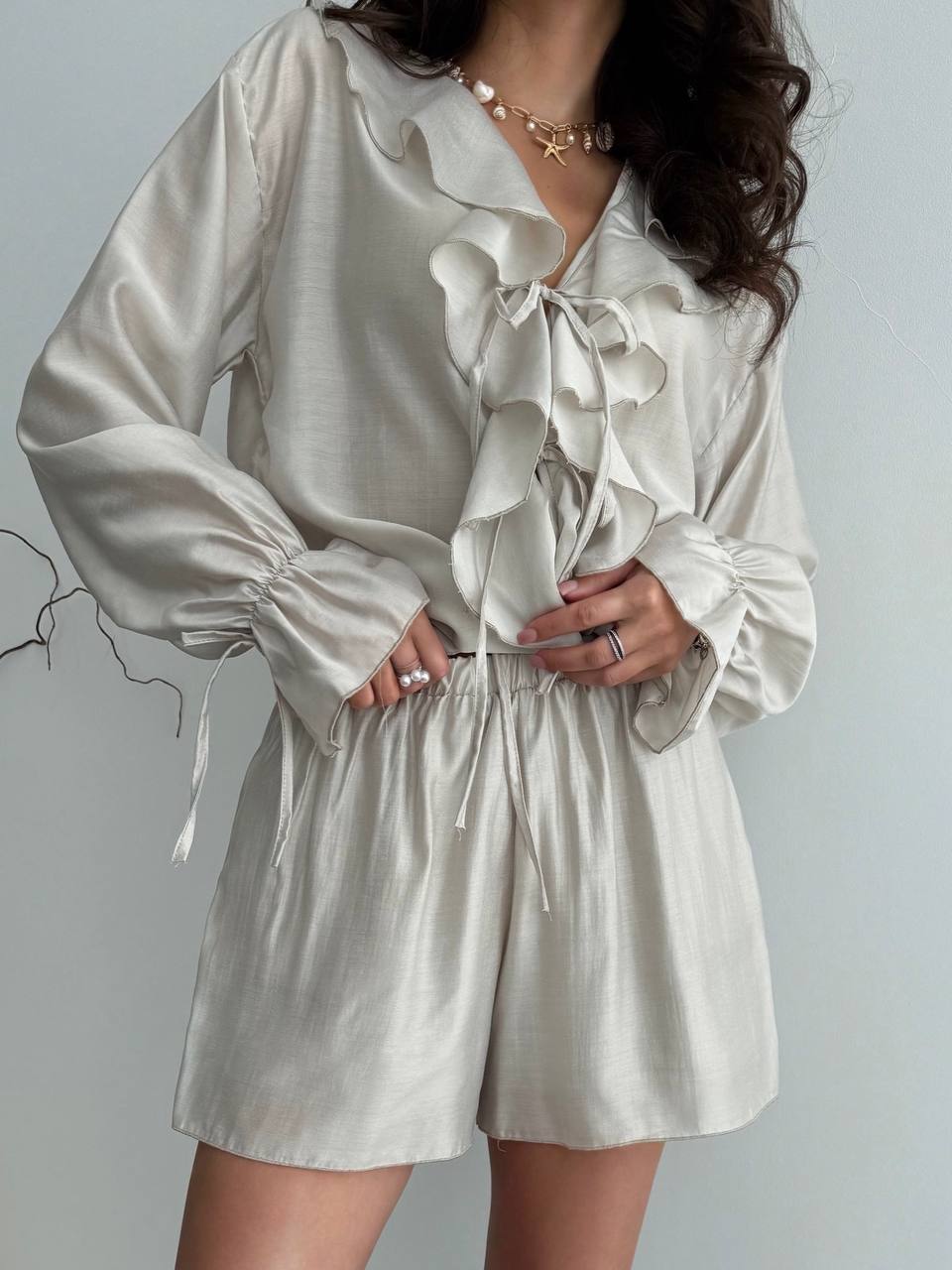 Woman wearing a beige ruffled blouse and shorts set against a plain background