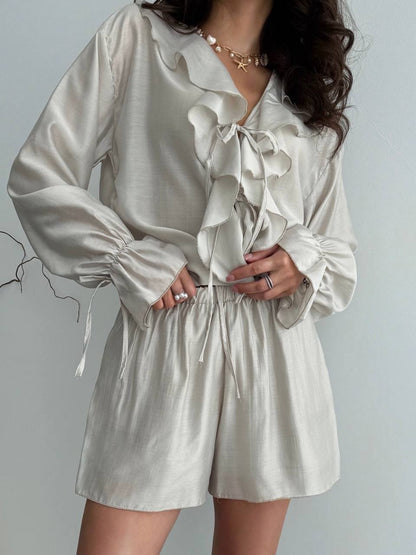 Woman wearing a beige ruffled blouse and shorts set against a plain background