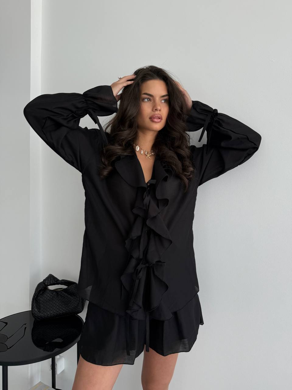 Woman wearing a black outfit with ruffled details against a white background