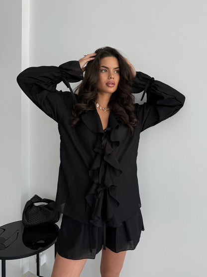 Woman wearing a black outfit with ruffled details against a white background