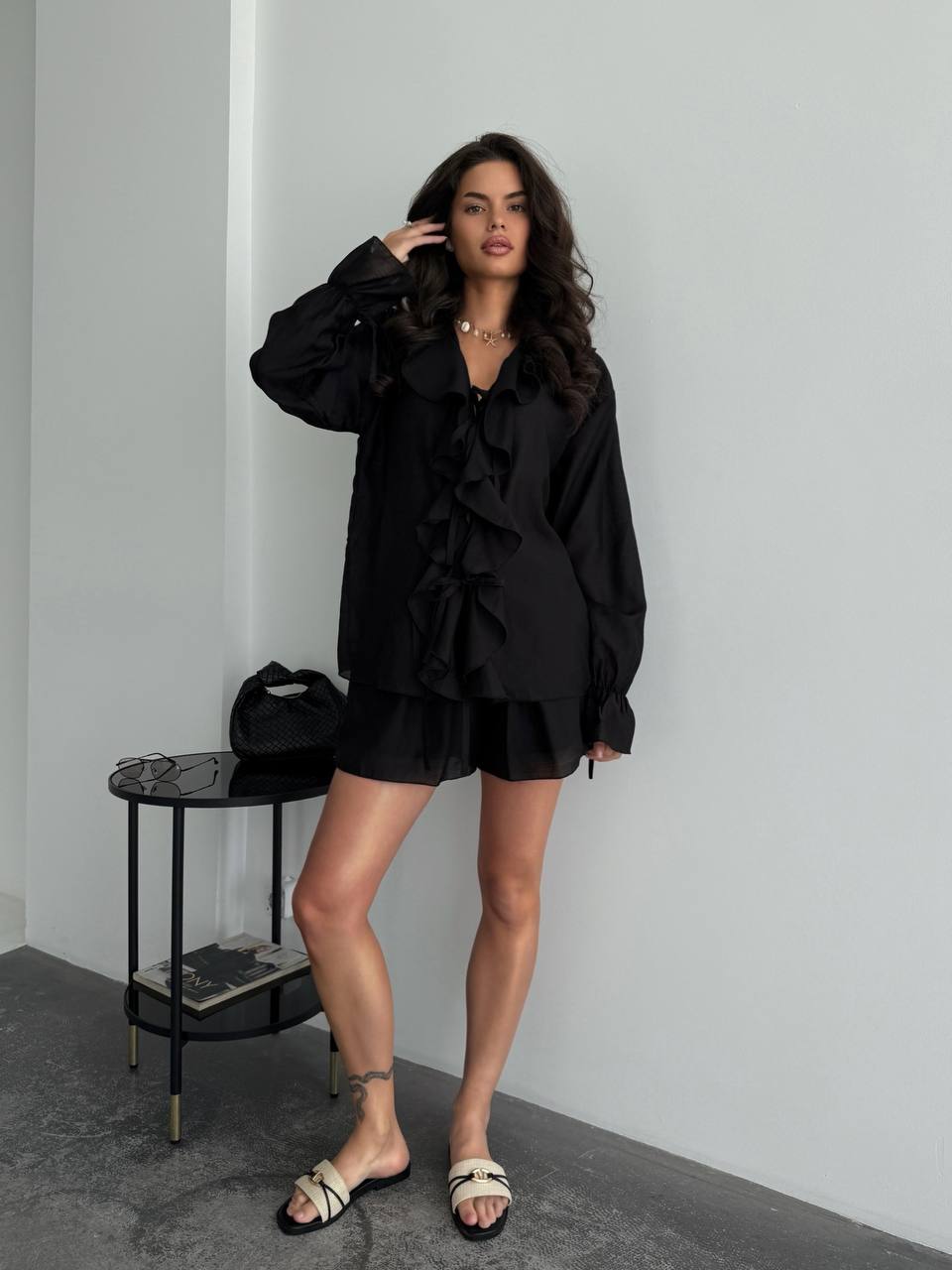 Woman wearing a black outfit standing against a plain wall.