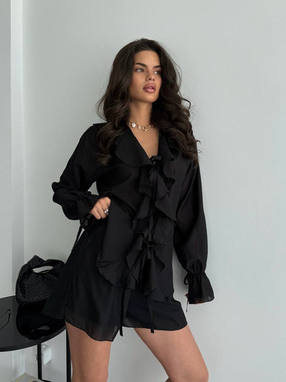 Woman wearing a black ruffled outfit against a plain background