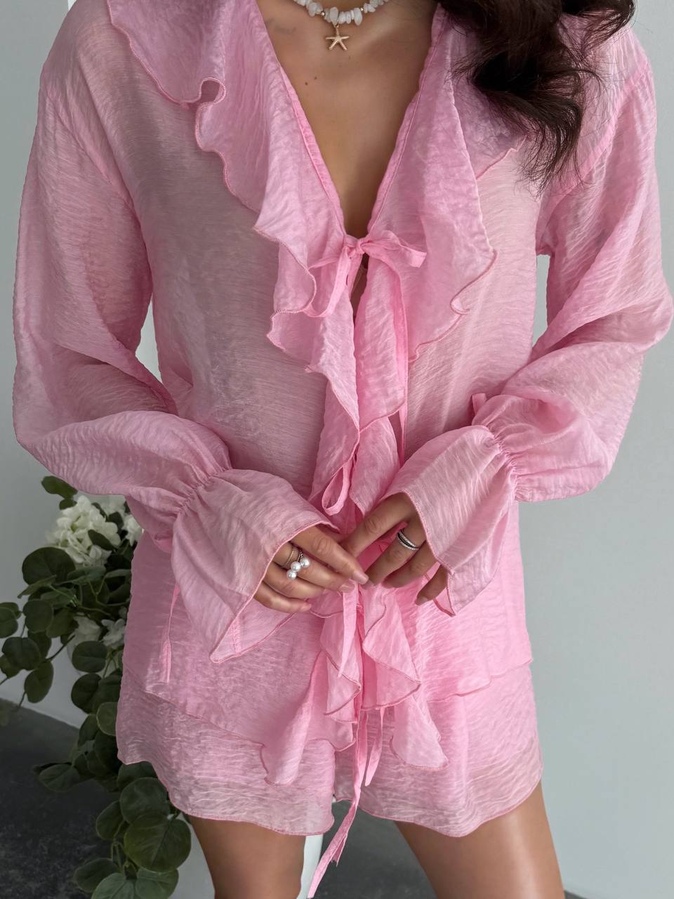 Person wearing a pink robe with ruffled details against a neutral background