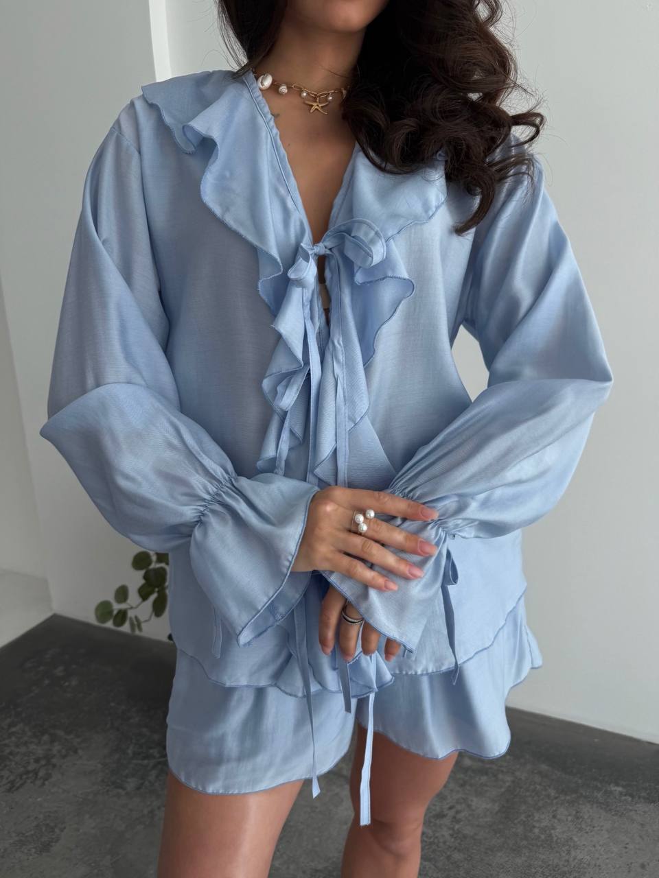 Woman wearing a light blue blouse with ruffled details and matching shorts.