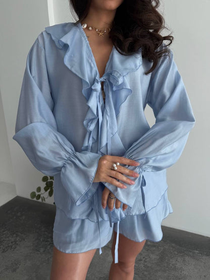 Woman wearing a light blue blouse with ruffled details and matching shorts.