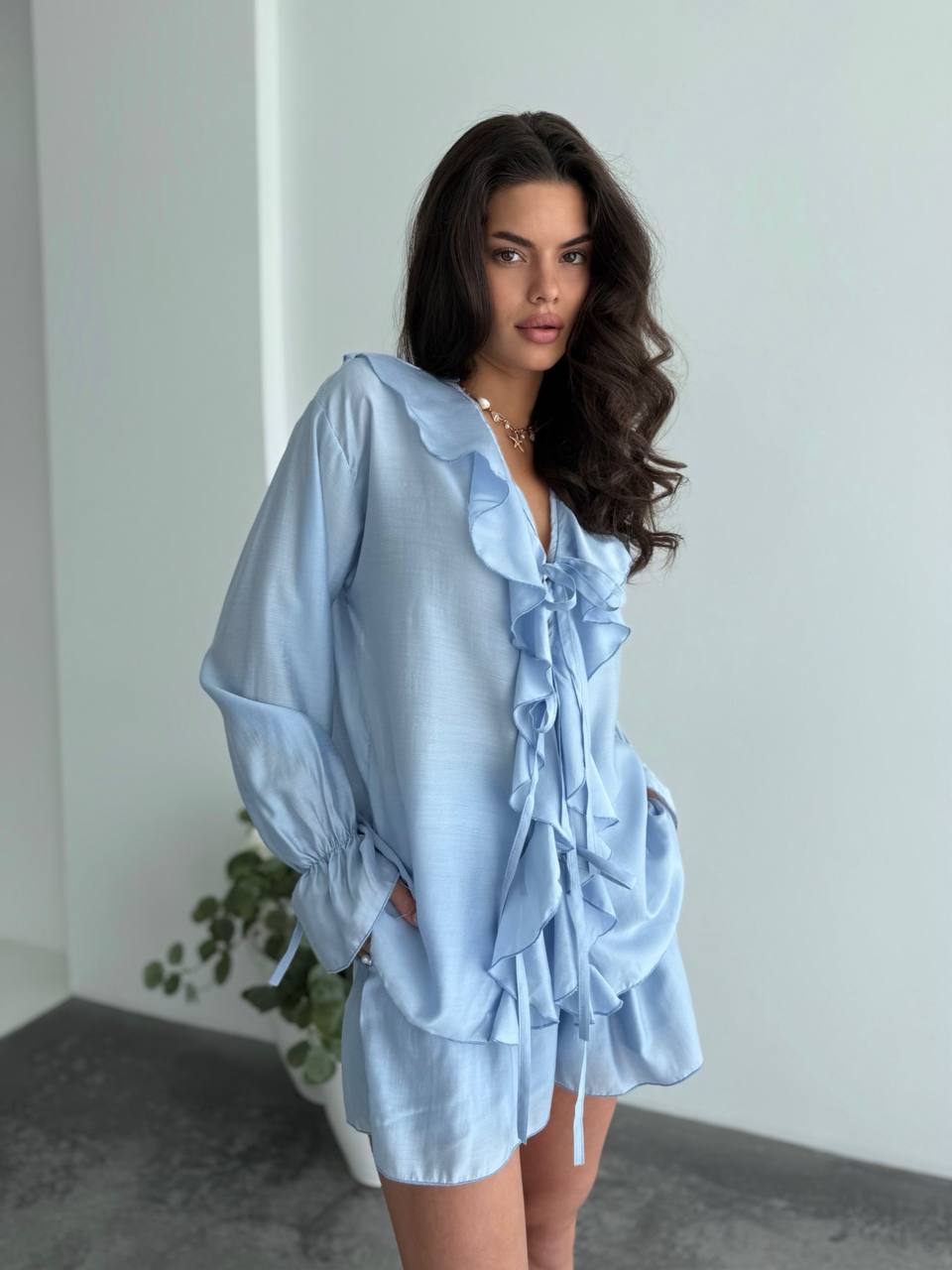 Woman wearing a light blue ruffled outfit against a plain background