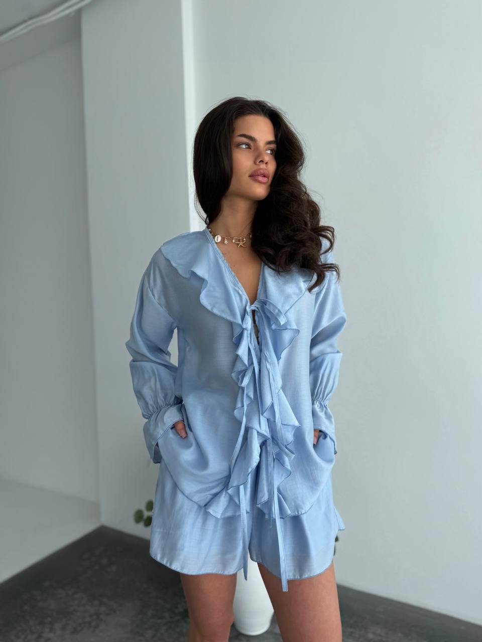Woman wearing a light blue dress with ruffled details against a plain background