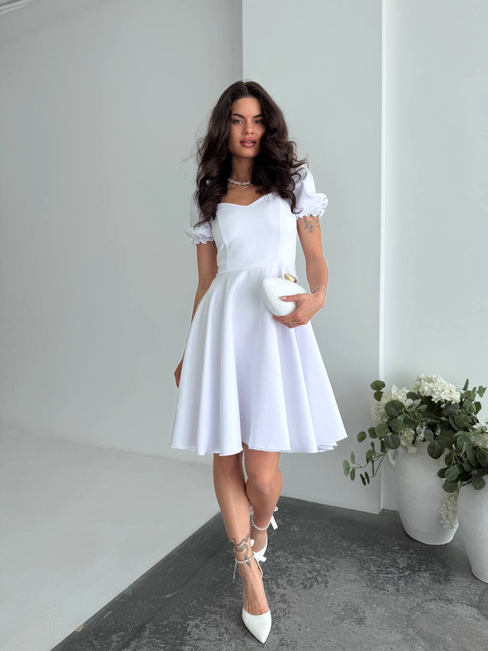 Woman in a white dress standing in a minimalistic room with a plant.