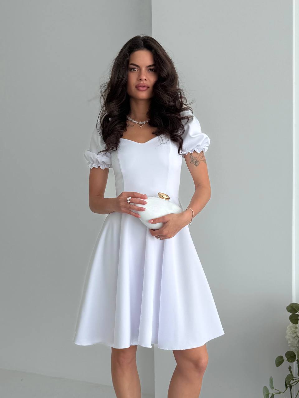 Woman wearing a white dress holding a clutch against a plain background